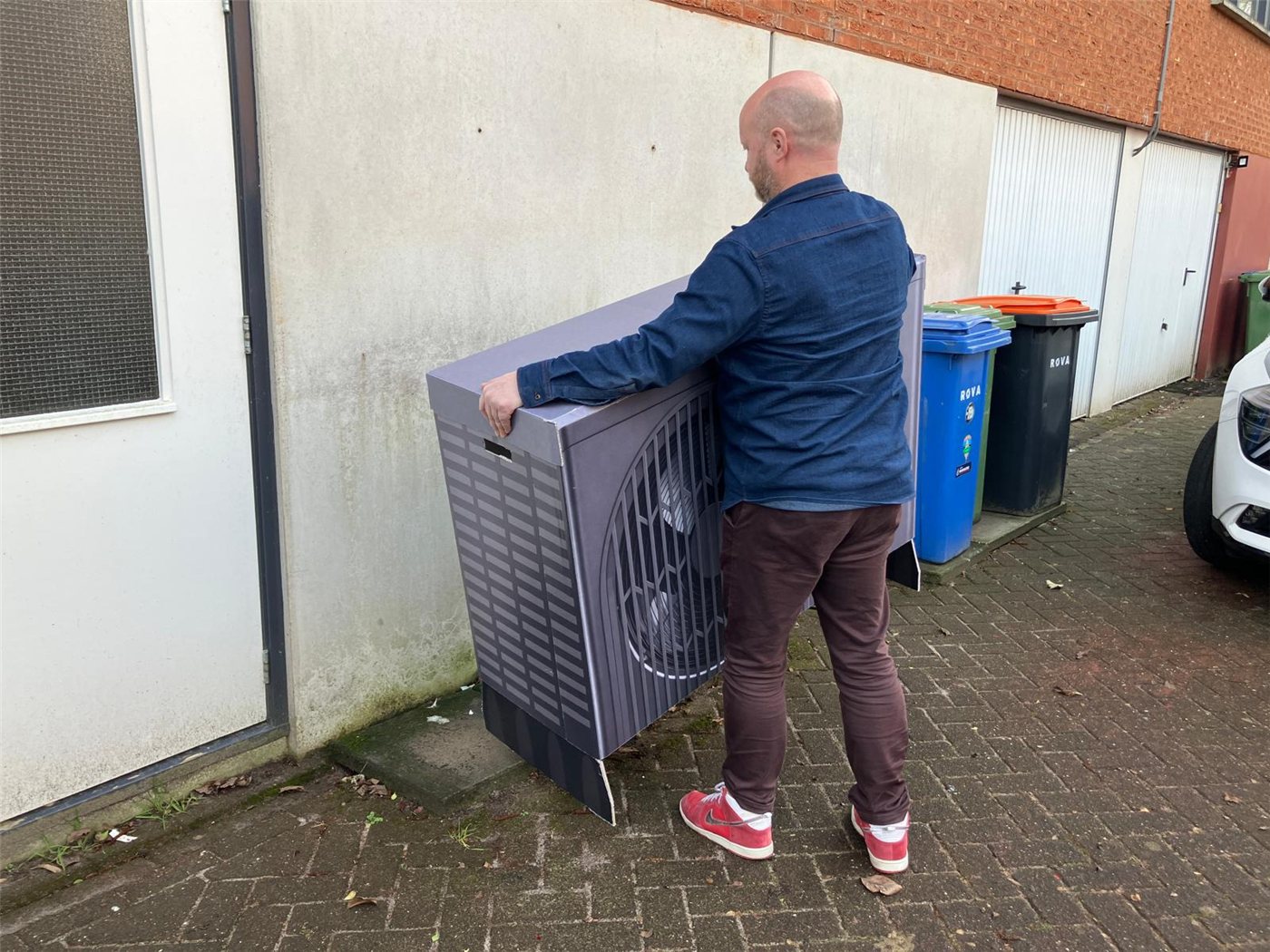 Bewoner plaatst een 1:1 kartonnen warmtepompmodel in de eigen woning